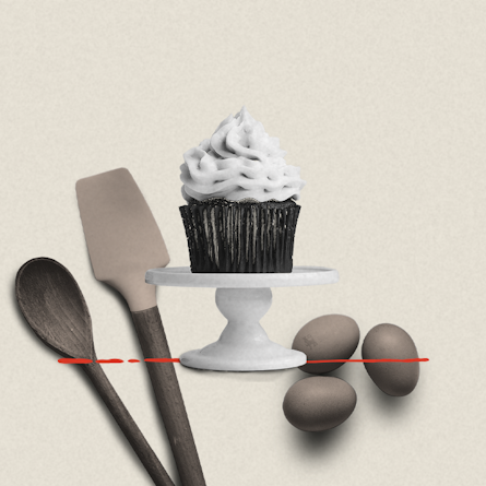 A cupcake on a serving tier with baking ingredients in the background.