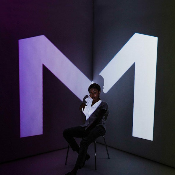 A film still of a person illuminated by a projected M.