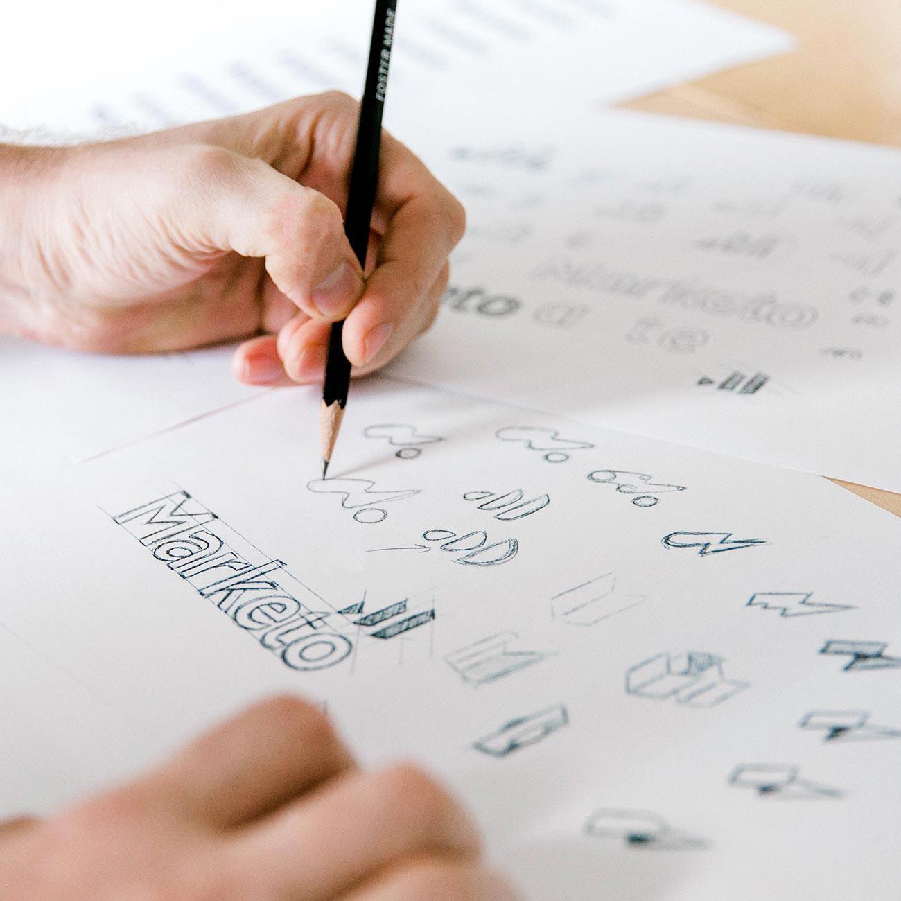 A hand sketches out ideas for Marketo's mark.